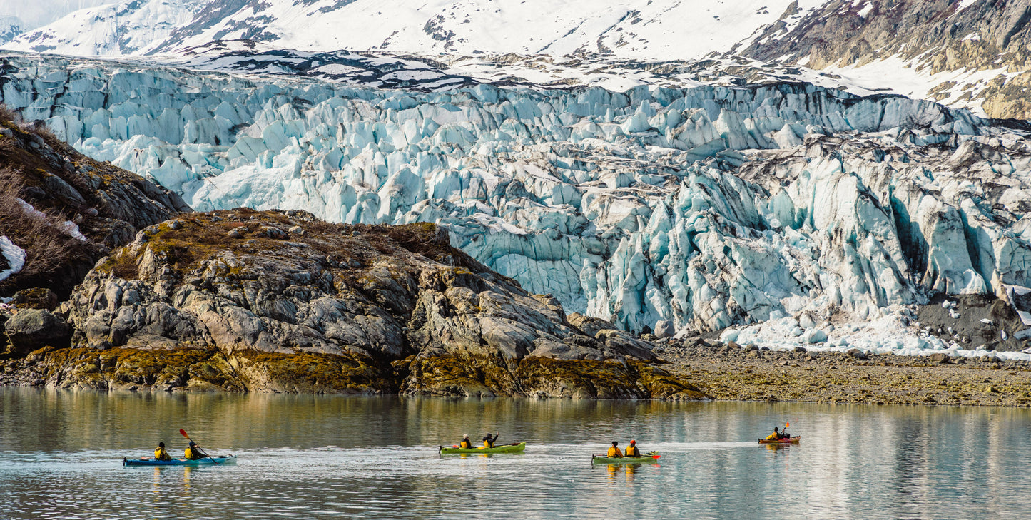 Four double kayaks paddling in front of a massive blue tidewater glacier