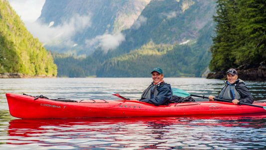 Two people in a red double kayak with tree-covered mountains in the background.-UnCruise Adventures 