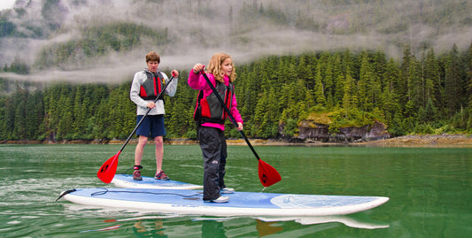 Daughter and father paddleboard in green water in front of a misty forest-UnCruise Adventures 